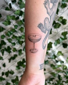 a person with a tattoo on their arm holding a wine glass and a cat in it