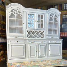 a white china cabinet sitting on top of a table next to a bookcase and rug