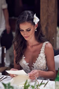 a woman sitting at a table writing in a note book with a flower in her hair