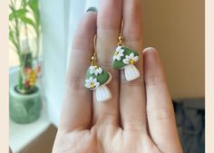 a person is holding two small green and white flowers on their earring wires,