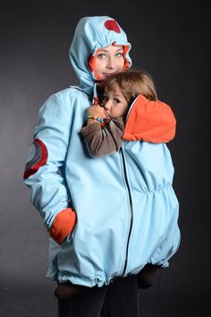 a woman in a blue jacket holding a small child wearing an orange and gray outfit