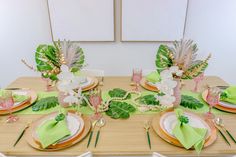 the table is set with green and white plates, silverware, and tropical leaves