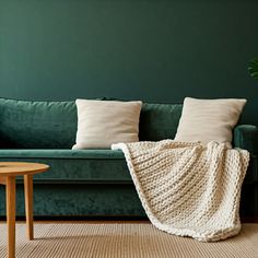 a green couch with two pillows and a blanket on it next to a small table