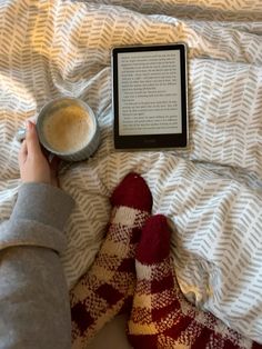 a person laying in bed with their feet up next to an electronic book and cup of coffee