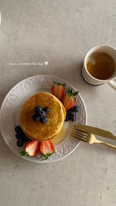 a plate with pancakes, strawberries and blueberries on it next to a cup of coffee