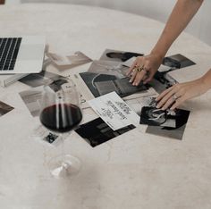 a table topped with pictures and a glass of red wine next to a laptop computer