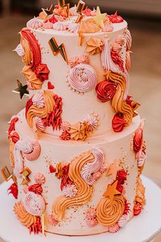 a three tiered wedding cake decorated with orange and pink icing, topped with stars