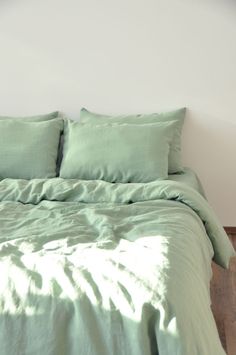 a bed with green sheets and pillows on top of it in front of a white wall