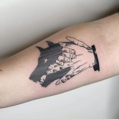 two hands holding each other over a black and white tattoo on the right arm,