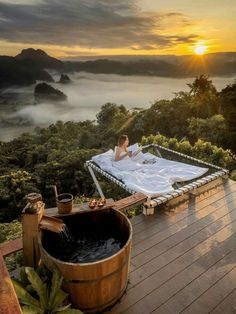 a woman laying in a hot tub on top of a wooden deck next to a forest