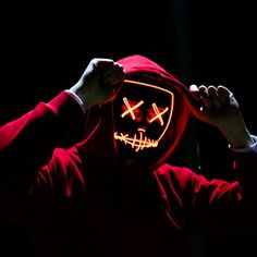 a person in a red hoodie is holding up a mask with two crosses on it