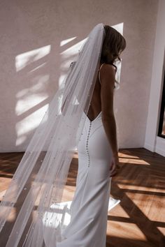 a woman in a white wedding dress is looking down at the floor with her veil over her head