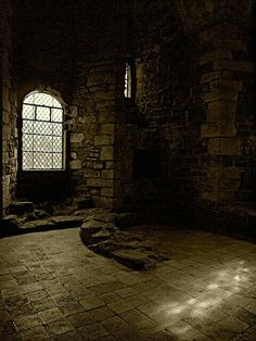 an empty room with stone walls and flooring in the dark, lit by sunlight coming through a window