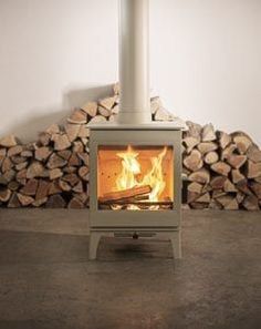 a fire place with logs stacked in the background and a white wall behind it,