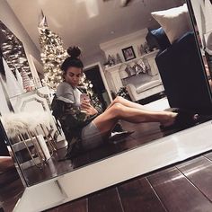 a woman sitting on the floor looking at her cell phone in front of a mirror