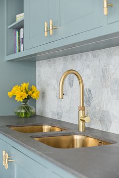 a kitchen with blue cabinets and gold faucets on the counter top, yellow flowers in vase next to the sink