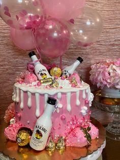 a cake with pink icing and balloons in the shape of champagne bottles on top