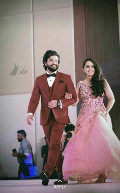 a man in a red suit and woman in a pink dress walking down the runway