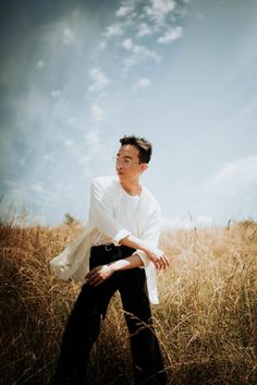 a man sitting on top of a tall grass covered field in front of a blue sky