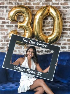 a woman sitting on top of a blue couch holding up a sign that says the one where victoria turns 30