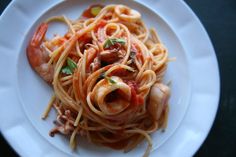 pasta with shrimp and tomato sauce on a white plate sitting on a black table top