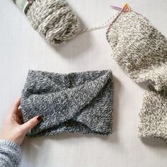 two knitted items are on the table with yarn in them and one is being held up by someone's hand