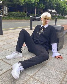 a young man sitting on the ground with his legs crossed, wearing a black shirt and tie