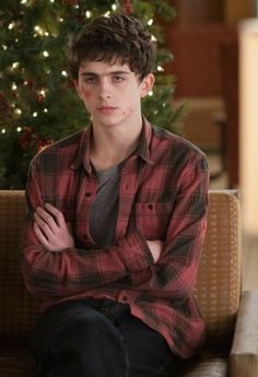 a young man is sitting on a couch in front of a christmas tree with his arms crossed