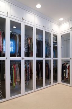 the closet is full of clothes and other items in white glass doors with lights on them