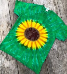 a green and yellow tie - dye shirt with a brown circle on the center, sitting on a wooden surface