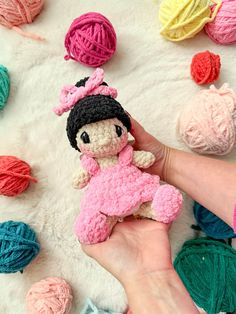 a hand holding a small crocheted doll next to balls of yarn