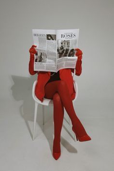 a woman sitting in a chair while reading a newspaper with her legs crossed and wearing red stockings