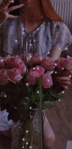 a woman sitting at a table with a vase filled with pink roses