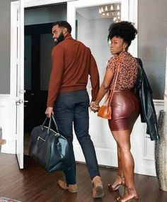 a man and woman holding hands while walking into a room with a handbag on the floor