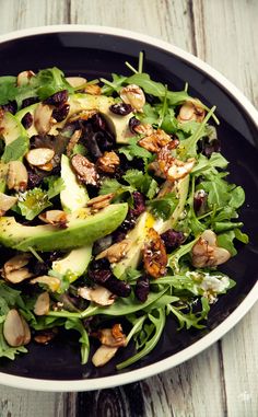 a salad with nuts, avocado and cranberries in a black bowl