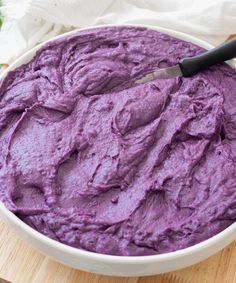 a white bowl filled with purple food on top of a wooden cutting board next to a knife