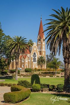 an old church surrounded by palm trees and trimmed with shrubs in the foreground, on a sunny day