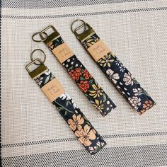 two straps with flowers on them are sitting on a tablecloth, one has a metal buckle and the other has a leather strap