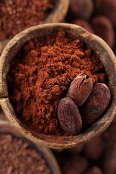 cocoa pods and powdered cocoa in a wooden bowl on top of other cocoa beans