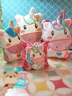 four stuffed unicorns sitting on top of a bed next to pillows and teddy bears