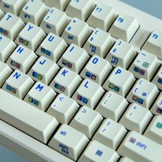 a close up view of a white keyboard with blue and green letters on the keys