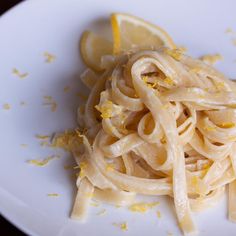 a white plate topped with pasta and lemon wedges