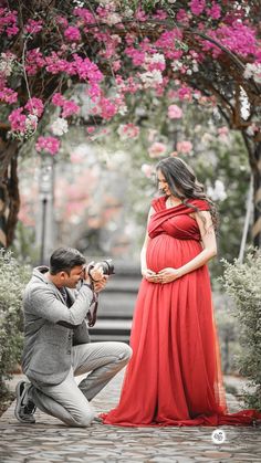 a man kneeling down next to a woman in a red dress and holding a camera