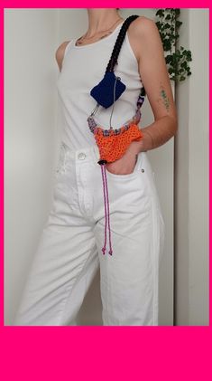 a woman in white pants holding an orange and blue purse with beads on the bottom