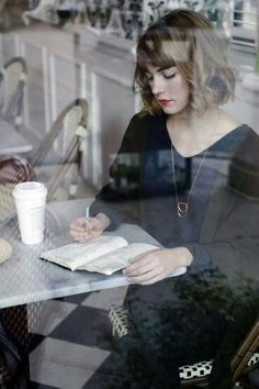 a woman sitting at a table with a book and coffee in front of her window