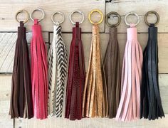 six different colors of leather tassels hanging on a wooden wall with metal rings