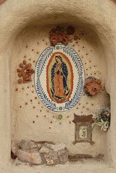 an image of the virgin mary on a stucco wall with flowers and rocks around it