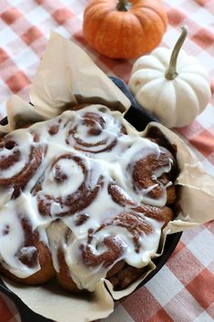 a pan filled with cinnamon rolls on top of a checkered table cloth next to pumpkins