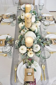 the table is set with white pumpkins, greenery and candles for an elegant centerpiece