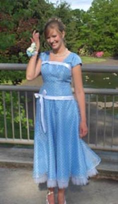 a woman in a blue dress is standing on a bridge and waving to the camera